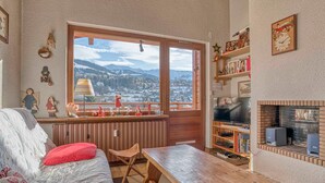 A cozy room with a large window, wooden furniture, a fireplace, and a bookshelf. - Cozy apartment with mezzanine in Megève, near ski slopes (Megève)