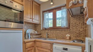 A kitchen with wooden cabinets, a Bosch oven, a dishwasher, and a window with lace curtains. - Cozy apartment with mezzanine in Megève, near ski slopes (Megève)
