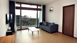 Een moderne woonkamer met een bank, een salontafel, een televisie en een groot raam met uitzicht op een landschap.