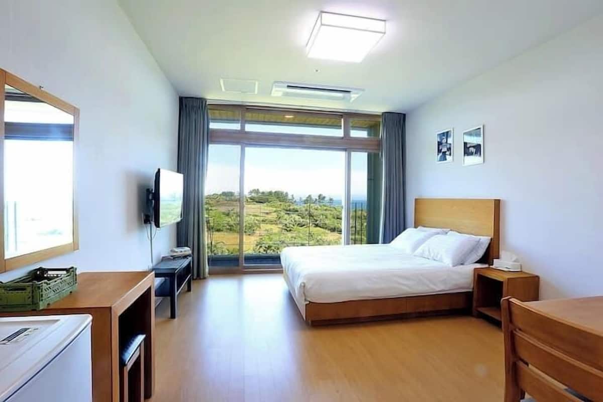 A hotel room with a bed, a desk, a television, and a large window offering a view of the outdoors.