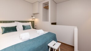 Ein modernes Hotelzimmer mit einem ordentlich bezogenen Bett, einem kleinen Nachttisch und einem an der Wand befestigten Kleiderschrank.