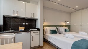 Ein modernes Hotelzimmer mit Küchenzeile, zwei Betten, einem Essbereich und einem Badezimmer.
