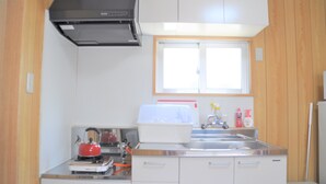 A compact kitchen with white cabinets, a stainless steel sink, a kettle, and a toaster. - Reiwa House (Ishigaki)