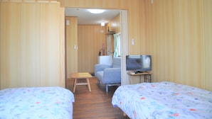 A hotel room with two beds, a television, a small table, and a bathroom visible through an open door. - Reiwa House (Ishigaki)