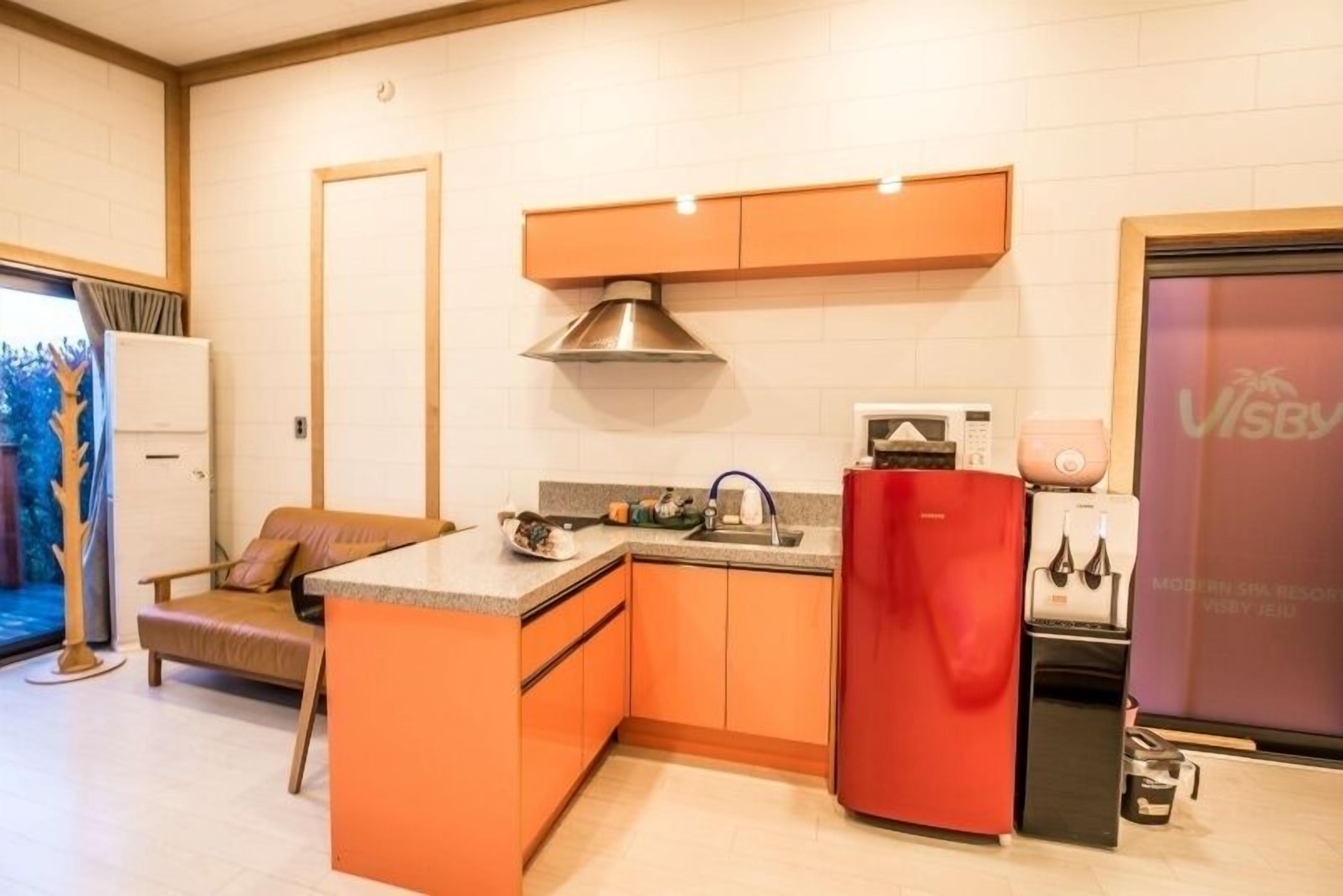 Una cocina compacta con gabinetes naranja, un refrigerador rojo y un microondas.