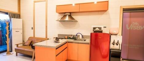 Una cocina compacta con gabinetes naranja, un refrigerador rojo y un microondas.