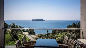 A balcony with wicker furniture overlooking a coastal view. - Visby Jeju Palm Village (Seogwipo)