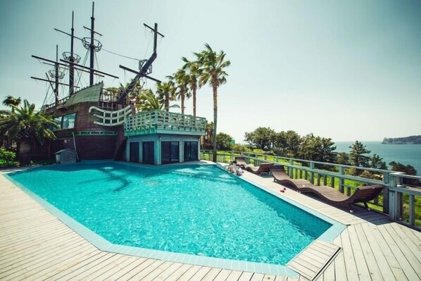 Una piscina con cubierta de madera, rodeada de palmeras y vista al mar.