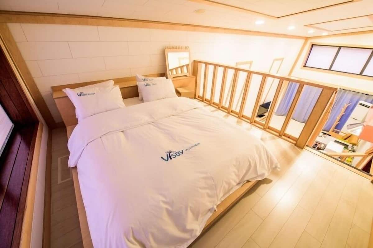 A hotel room with a bed, a wooden headboard, a nightstand, a mirror, and a window with curtains.