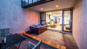 A modern outdoor patio with a hot tub, seating area, and a glimpse of the interior through a glass door. - Visby Jeju Palm Village (Seogwipo)