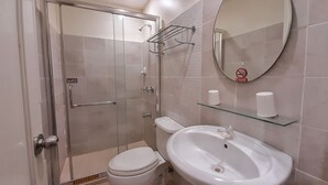 Un baño moderno con cabina de ducha de vidrio, inodoro, lavamanos y espejo.