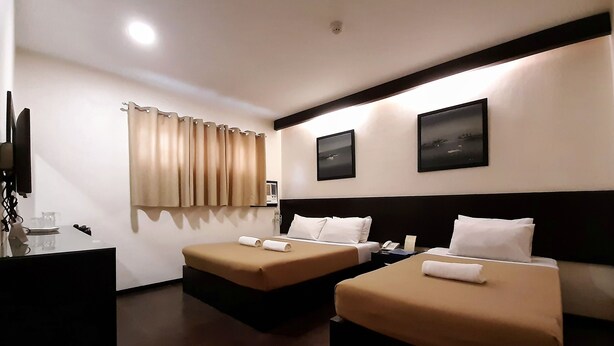 Una habitación de hotel con dos camas individuales, un escritorio con teléfono y una televisión montada en la pared.