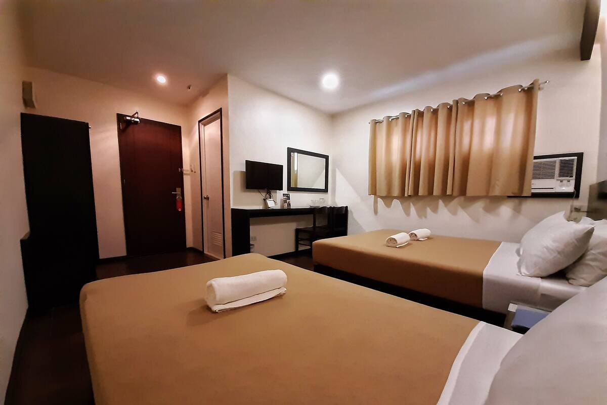 A hotel room with two beds, a desk with a computer, a mirror, and a wall-mounted air conditioner.