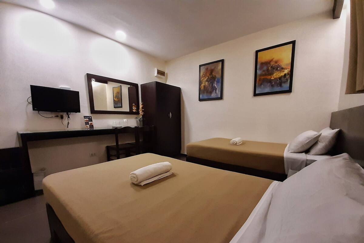 A hotel room with a bed, a desk, a chair, a TV, and two paintings on the wall.