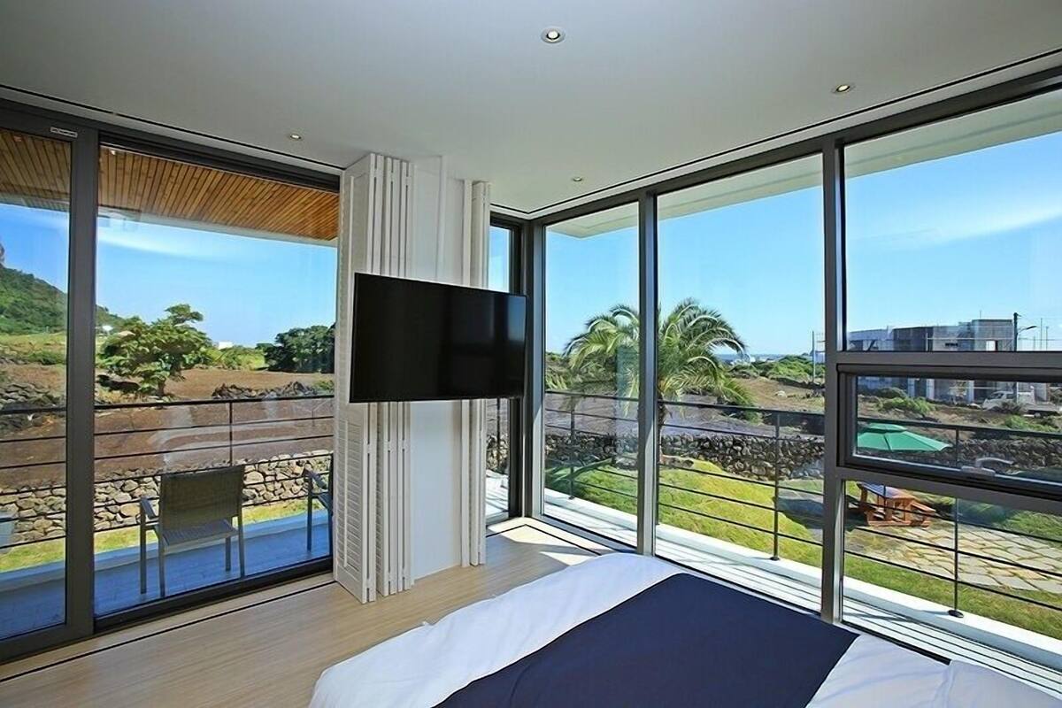 Ein modernes Schlafzimmer mit einem großen Bett, einem flachbildfernseher an der Wand und einem Balkon mit Blick auf die Landschaft.