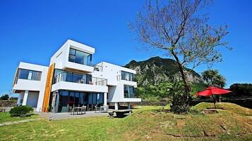 Uma casa moderna de dois andares, com grandes janelas, uma varanda e vista para uma montanha.