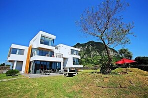 Ein modernes, zweistöckiges Haus mit großen Fenstern, einem Balkon und Blick auf einen Berg.