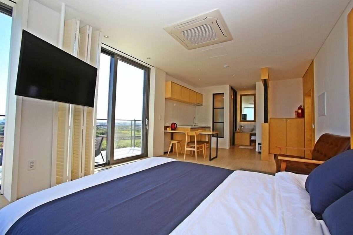 Ein modernes Schlafzimmer mit einem großen Bett, einem an der Wand montierten Fernseher und einer Schiebetür, die auf einen Balkon führt.