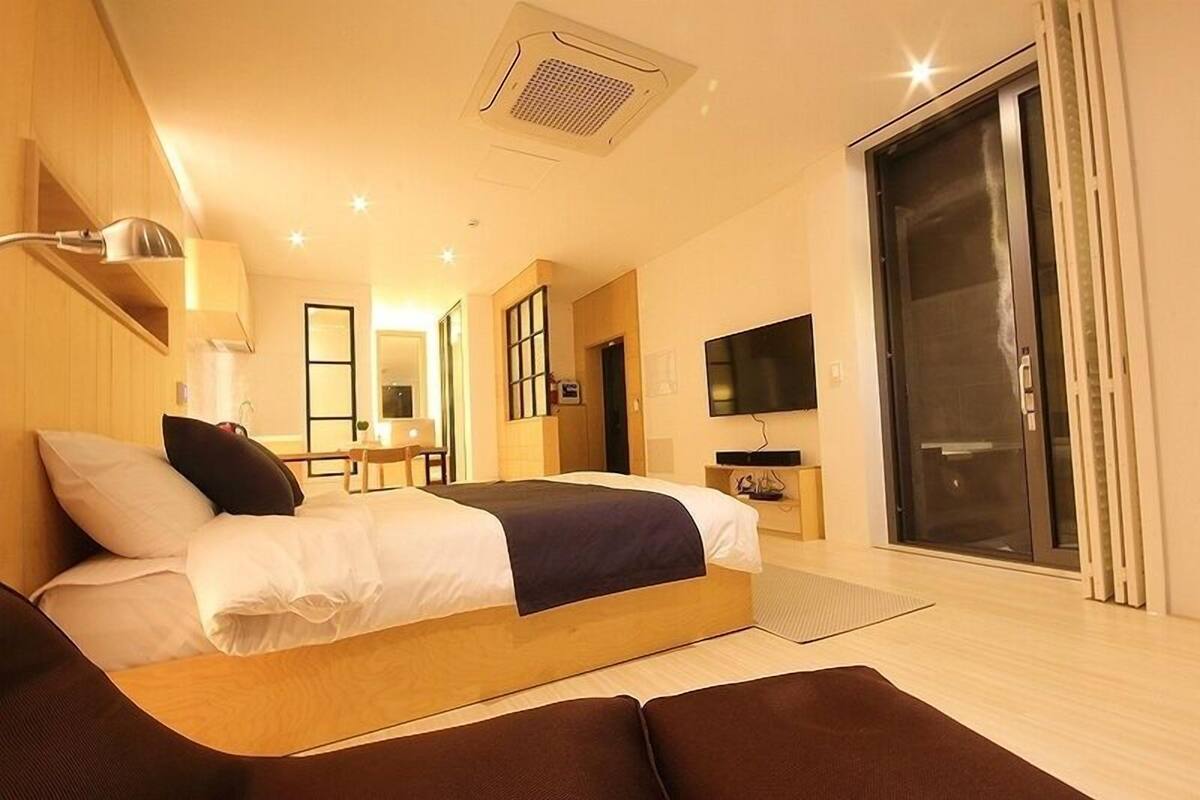 Ein modernes Hotelzimmer mit einem großen Bett, einem Schreibtisch, einem Fernseher und einer Schiebetür.