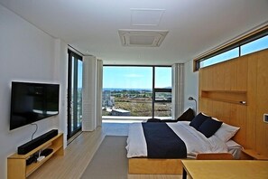 Ein modernes Hotelzimmer mit einem großen Bett, einem Flachbildfernseher, einem Holztisch und Blick auf die Stadt durch große Fenster.