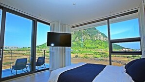 A bedroom with a large bed, a TV, and a balcony with chairs. - Villanoi Jeju (Seogwipo)