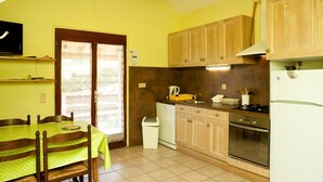 A kitchen with wooden cabinets, a stove, a refrigerator, and a dining table with chairs. - the gites of Manavit-haut T3 (occitanie)
