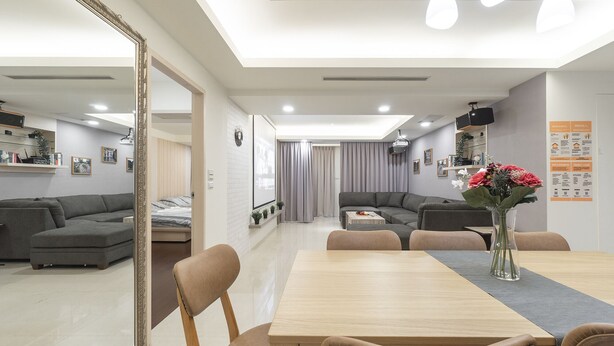 Ein modernes Wohnzimmer mit einem großen Spiegel, grauen Sofas, einem Holzesstisch und einer Vase mit Blumen.