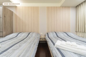 A 2nd bedroom with two beds, a wooden wardrobe, and a small bench.