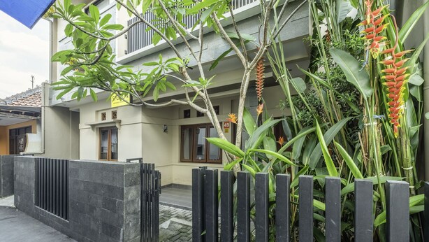 A two-story building with a balcony, surrounded by lush greenery and a black metal fence. - SPOT ON 2080 Rumah Kita Residence (Tasikmalaya)