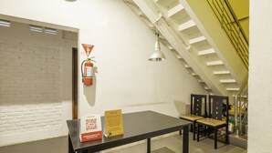 A room with a black table, two chairs, a QR code sign, a fire extinguisher, and a staircase. - SPOT ON 2080 Rumah Kita Residence (Tasikmalaya)