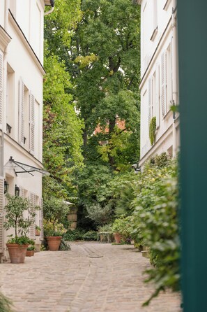 A narrow cobblestone street flanked by buildings with white facades and shutters, lined with potted plants and trees. - Hôtel des Grandes Ecoles (Paris)