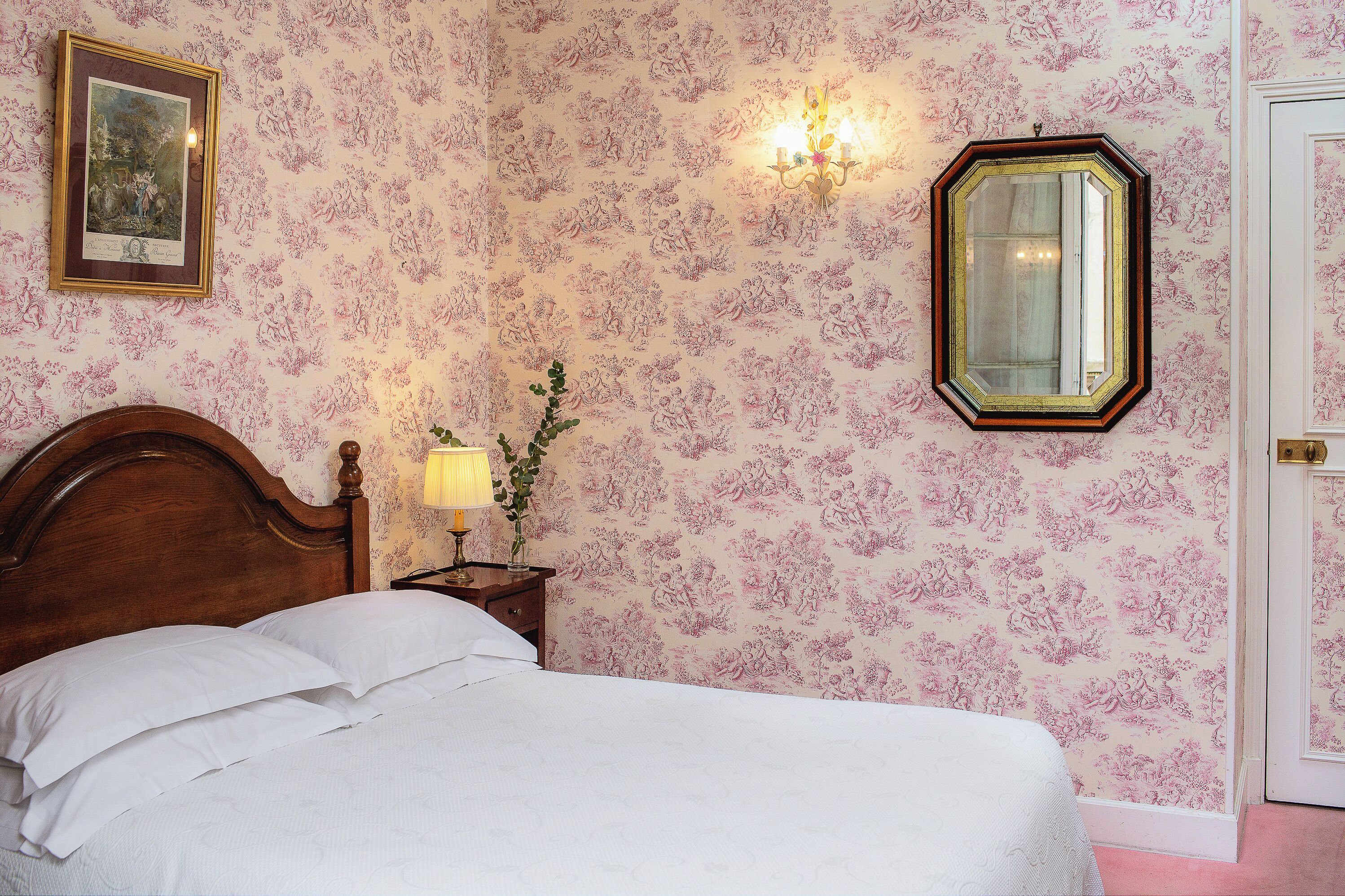 Une chambre à coucher avec un lit en bois, une table de chevet avec une lampe, un tableau encadré au mur et un miroir.