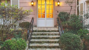 A two-story building with a pink facade, white shutters, and a stone staircase leading to the entrance.
