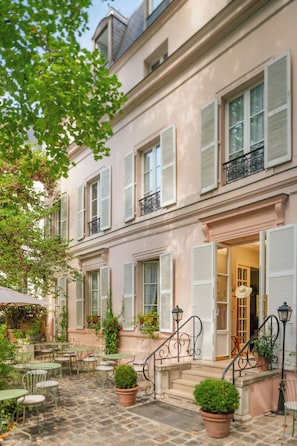 A building with a stone facade, multiple windows with shutters, outdoor seating, and potted plants. - Hôtel des Grandes Ecoles (Paris)