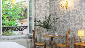 A room with a window, a table with chairs, a vase with greenery, and a wall with a detailed pattern.