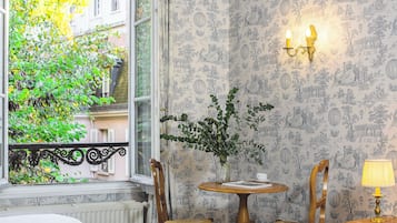A room with a view of a tree outside a window, a table with chairs, and a wall with a detailed pattern.
