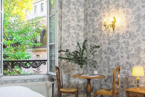 A room with a window, a table with chairs, a vase with greenery, and a wall with a detailed pattern. - Hôtel des Grandes Ecoles (Paris)