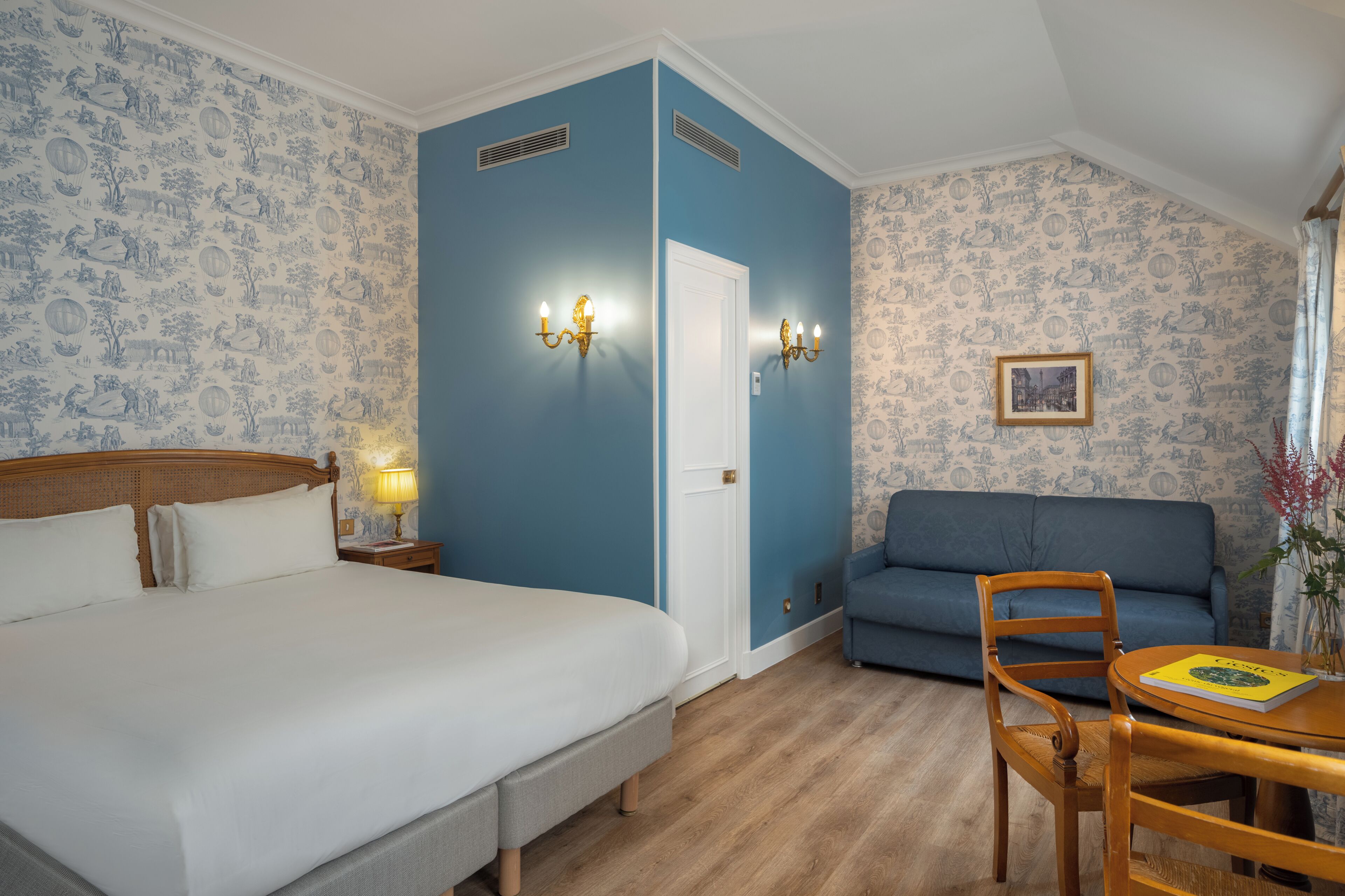 A hotel room with a bed, a sofa, a table with a book, and a wall with patterned wallpaper.