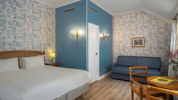A hotel room with a bed, a sofa, a table with a book, and a wall with patterned wallpaper.