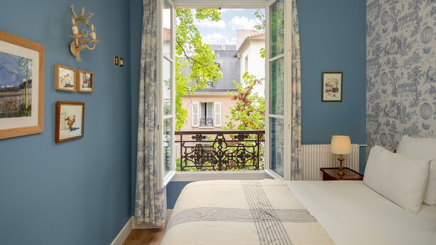 A bedroom with a large window, a bed, a nightstand, and wall-mounted artwork. - Hôtel des Grandes Ecoles Quartier Latin (Paris)