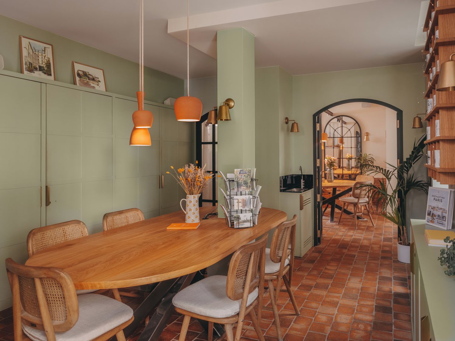 A dining area with a wooden table and chairs, a vase with flowers, and a bookshelf with books.