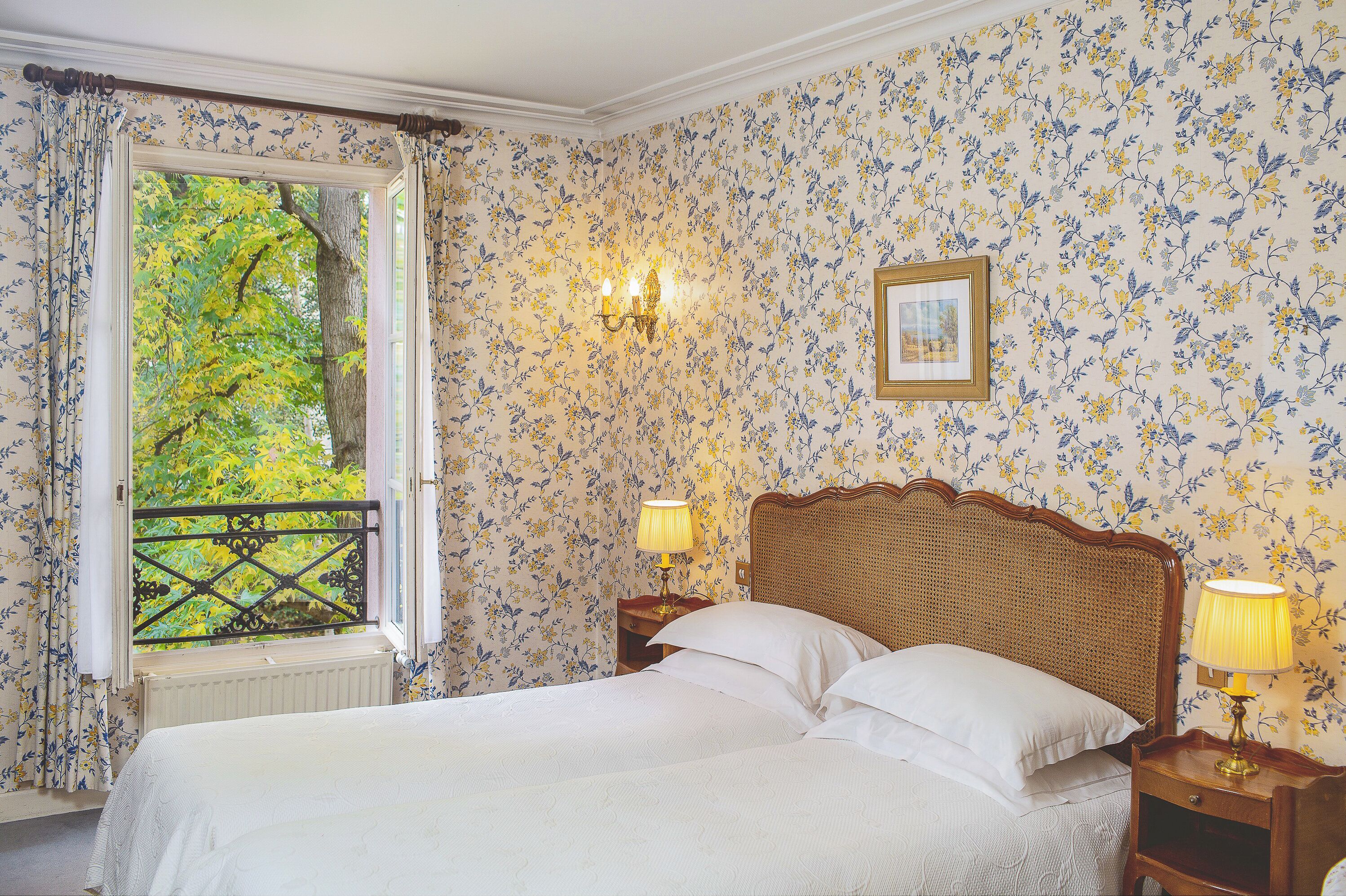 Ein Schlafzimmer mit großem Fenster, einem Bett mit weißen Leinentüchern, zwei Nachttischlampen und einem gerahmten Bild an der Wand.