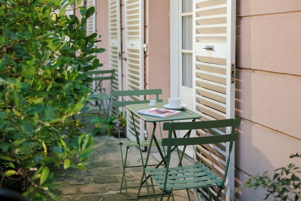 A narrow outdoor corridor with a table and chairs, a book, and a cup. - Hôtel des Grandes Ecoles Quartier Latin (Paris)
