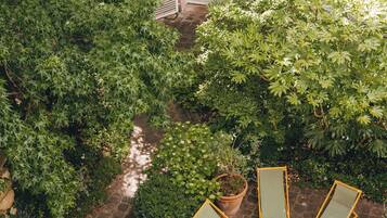 A courtyard with a table and chairs, surrounded by greenery and a building with shutters.