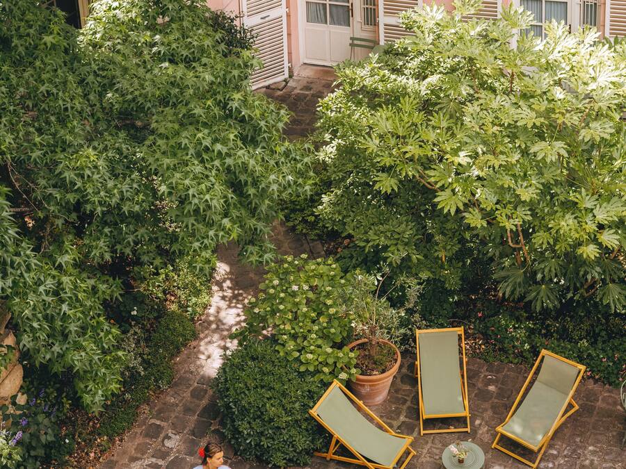 A courtyard with a table and chairs, surrounded by greenery and a building with shutters.