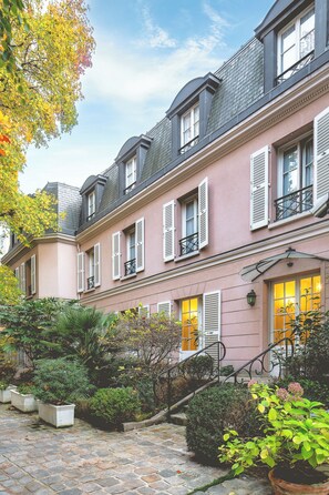 A multi-story building with a pink facade, white shutters, and a stone-paved courtyard. - Hôtel des Grandes Ecoles Quartier Latin (Paris)