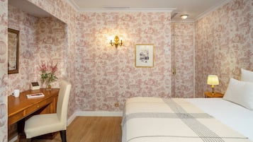 Ett hotellrum med en säng, ett skrivbord, en stol, ett nattduksbord och en väggmonterad lampa.