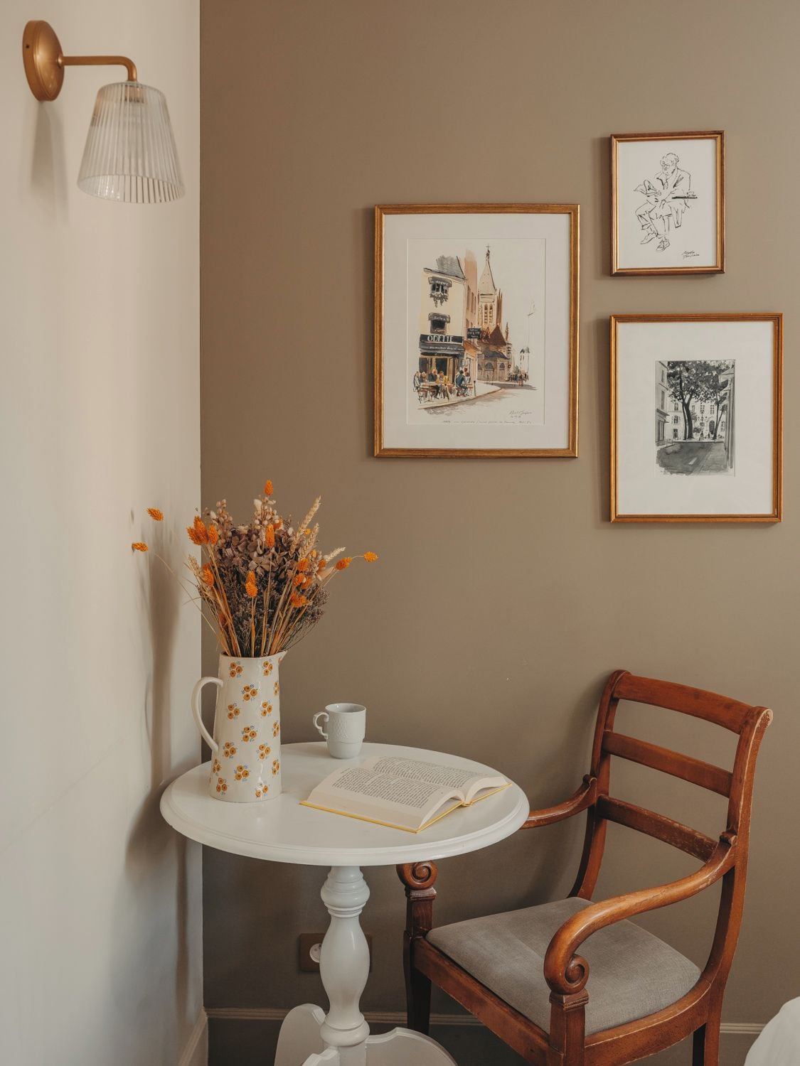 Una habitación con una mesa redonda, una silla, un florero con flores y cuadros en la pared.