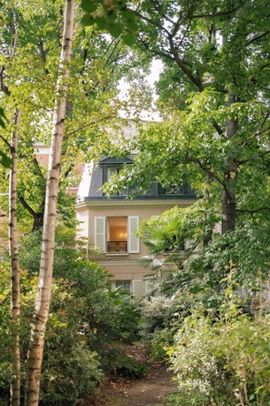 A two-story house with a balcony, surrounded by lush greenery and trees. - Hôtel des Grandes Ecoles (Paris)