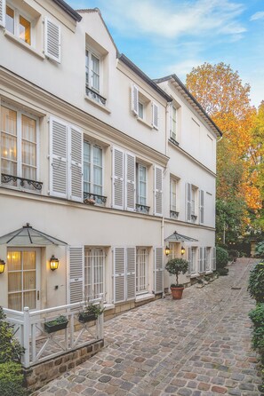 A two-story building with white exterior walls, shutters, and a cobblestone pathway. - Hôtel des Grandes Ecoles (Paris)